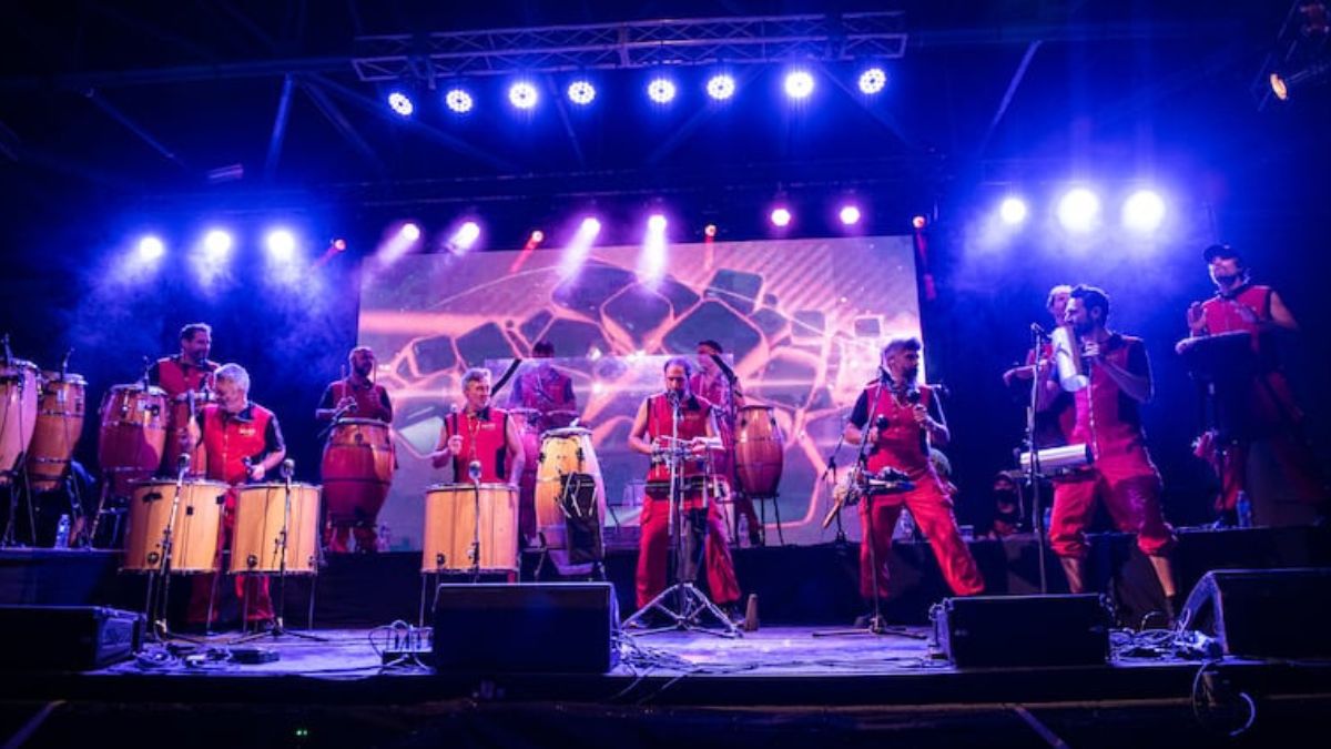 La Bomba de Tiempo en escena, varios percusionistas con tambores y luces violetas durante un show en vivo